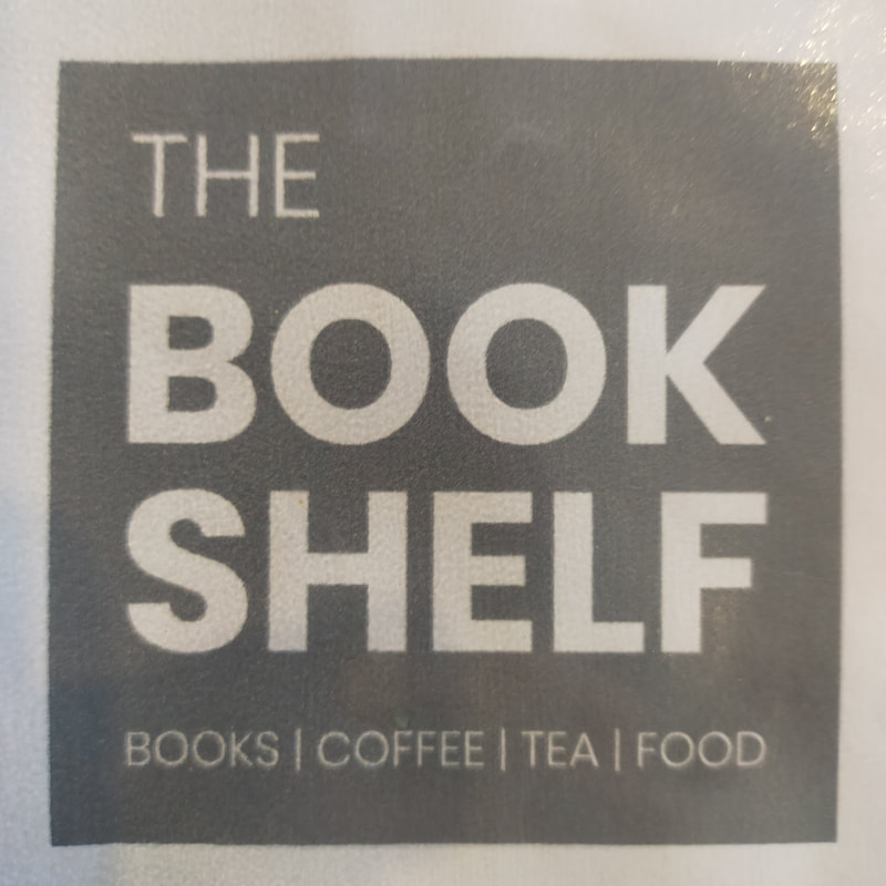 Picture shows the shop sign for the Bookshelf. The sign says The Bookshelf. Books, coffee, tea, food
