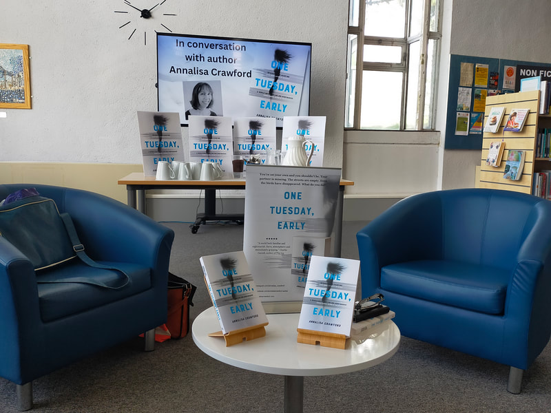 Photo shows a large display of books at Saltash Library, alongside two blue bucket chairs where the author and library manager sat for a question and answer session with guests.