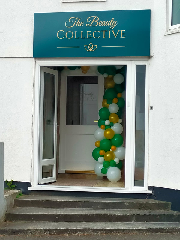 Picture shows the doorway of the Beauty Collective beauty salon with a display of green, gold, and white balloons.